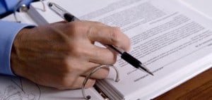 A hand holding a pen over a binder of documents