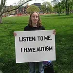 person holding a sign reading: Listen to me. I have autism.
