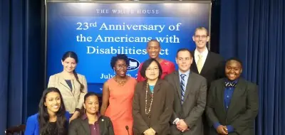 Group of people in front of a screen reading "23rd Anniversary of the Americans with Disabilities Act"