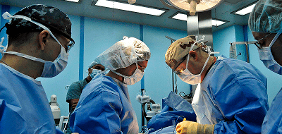 Four people wearing blue medical scrubs and face masks performing surgery