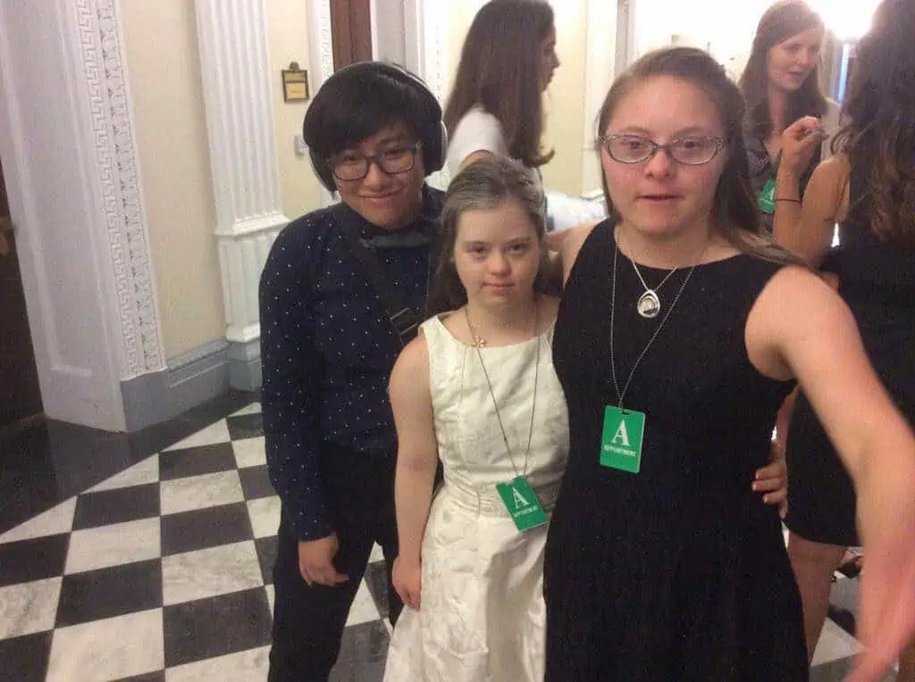 [Elly smiles and stands with Megan Bomgaars and Devon Adelman from the Global Down Syndrome Foundation.]