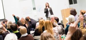 constituents raising their hands to ask questions at a congresspersons town hall meeting