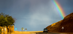 A rainbow emerges over a road after a storm