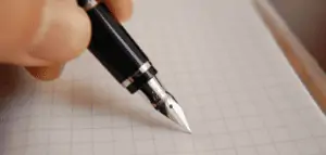 a white hand holds a black fountain pen against grid paper